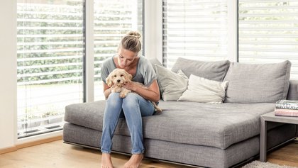 Frau sitzt mit kleinem Hund auf Sofa vor Raffstore